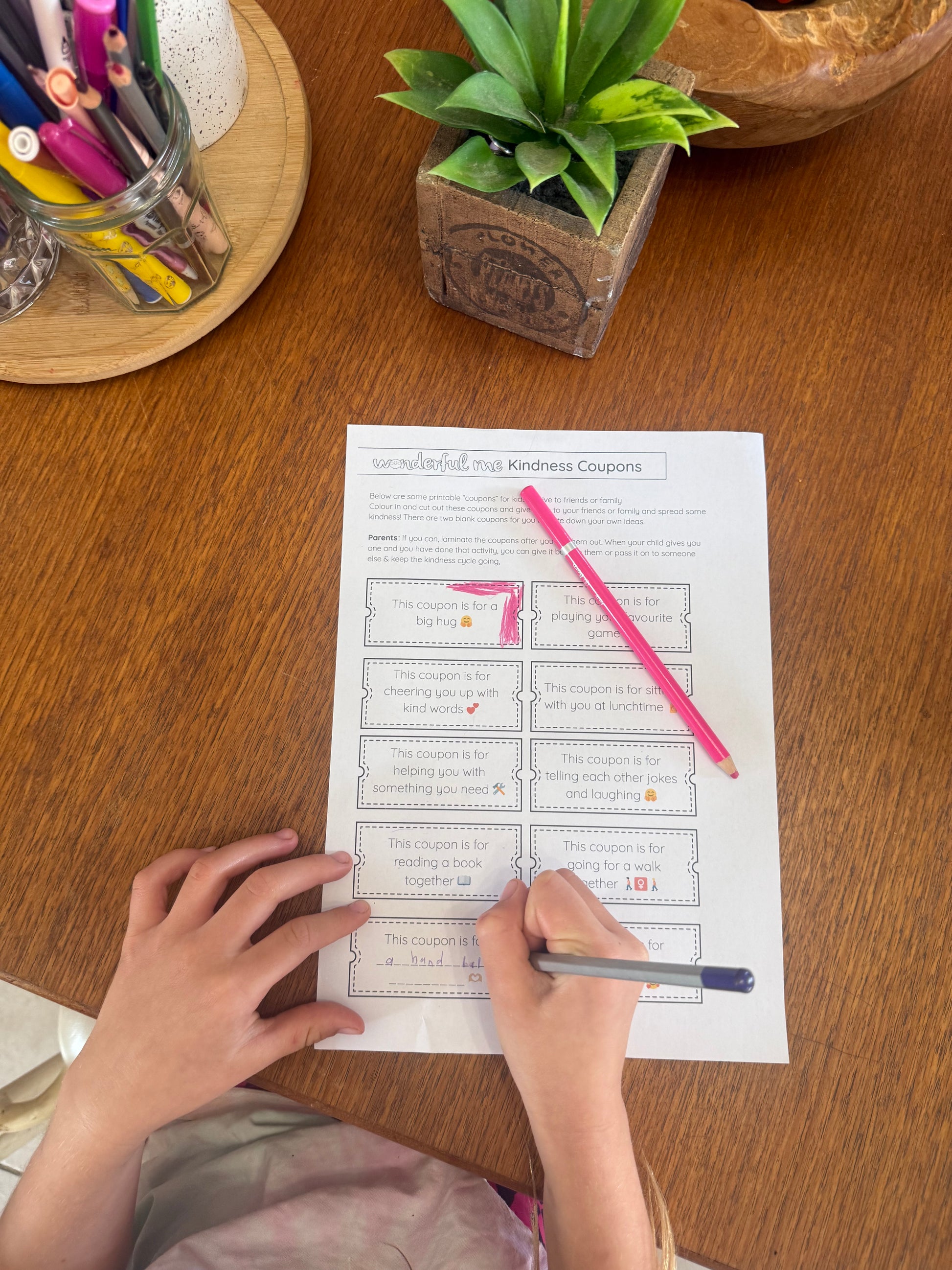 Person filling out a worksheet with a pink pen on a wooden table.